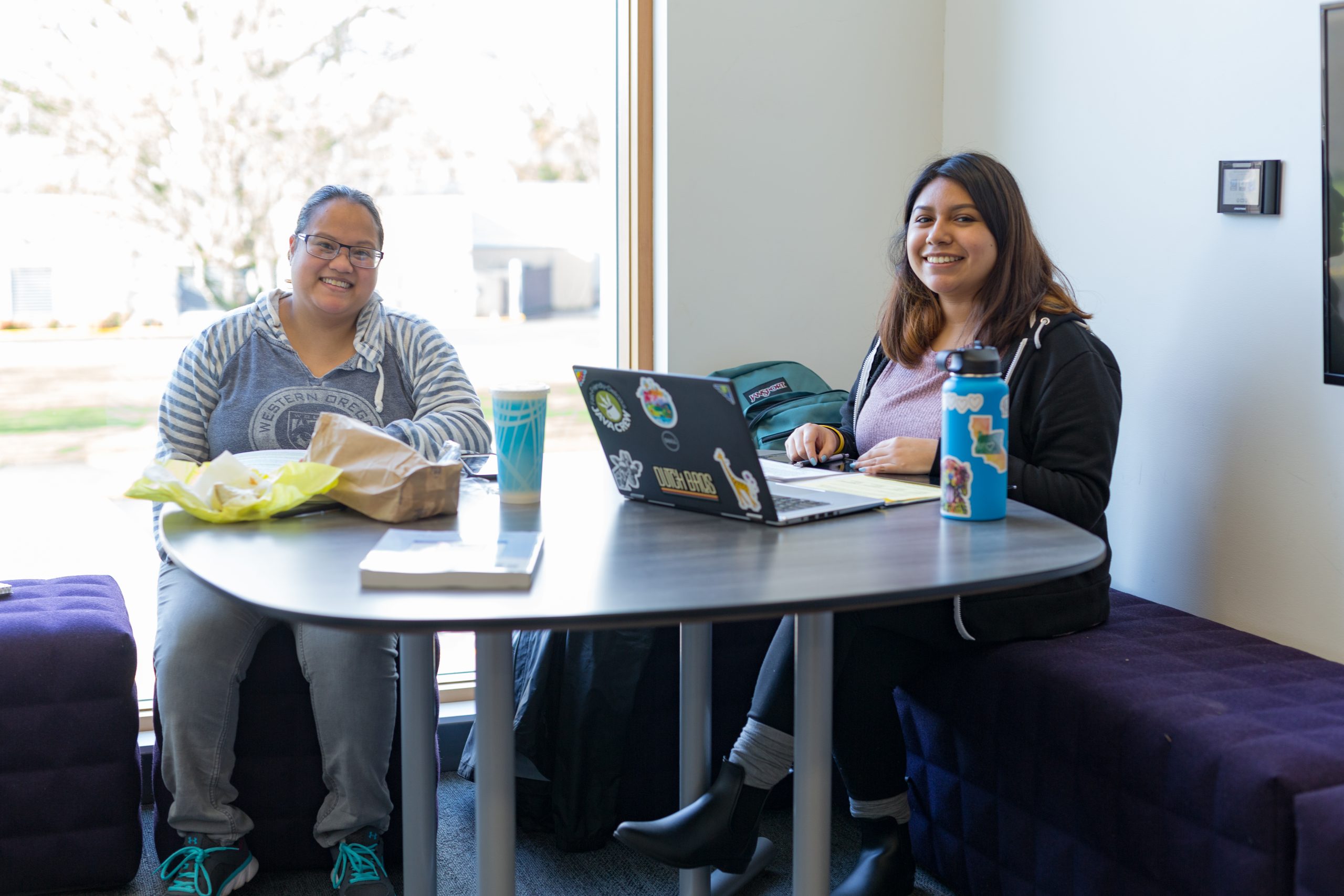 Two female students working together at window tables in RWEC. WOU Wolves Logo