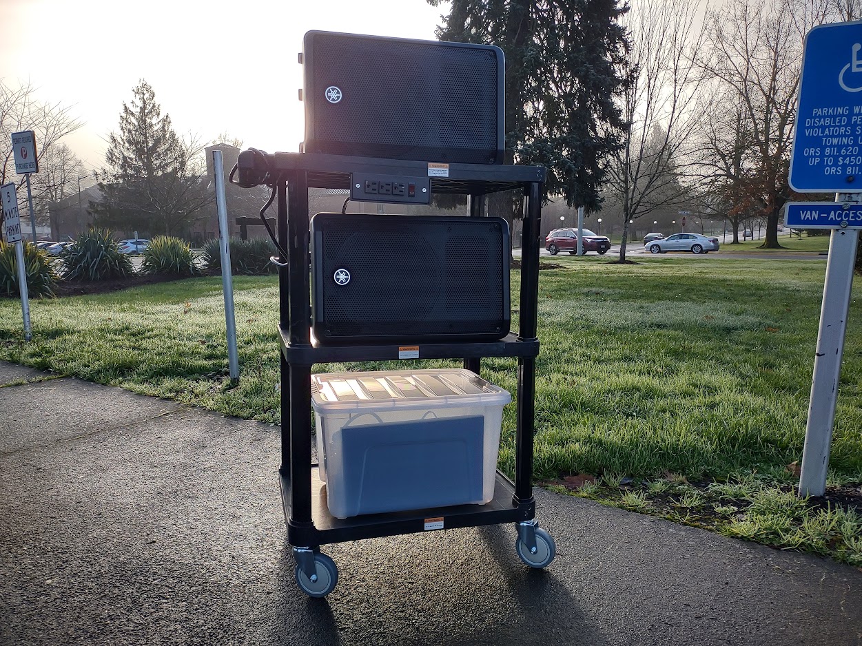 Plastic hand cart with two large speakers and a tote box full of cables and equipment.
