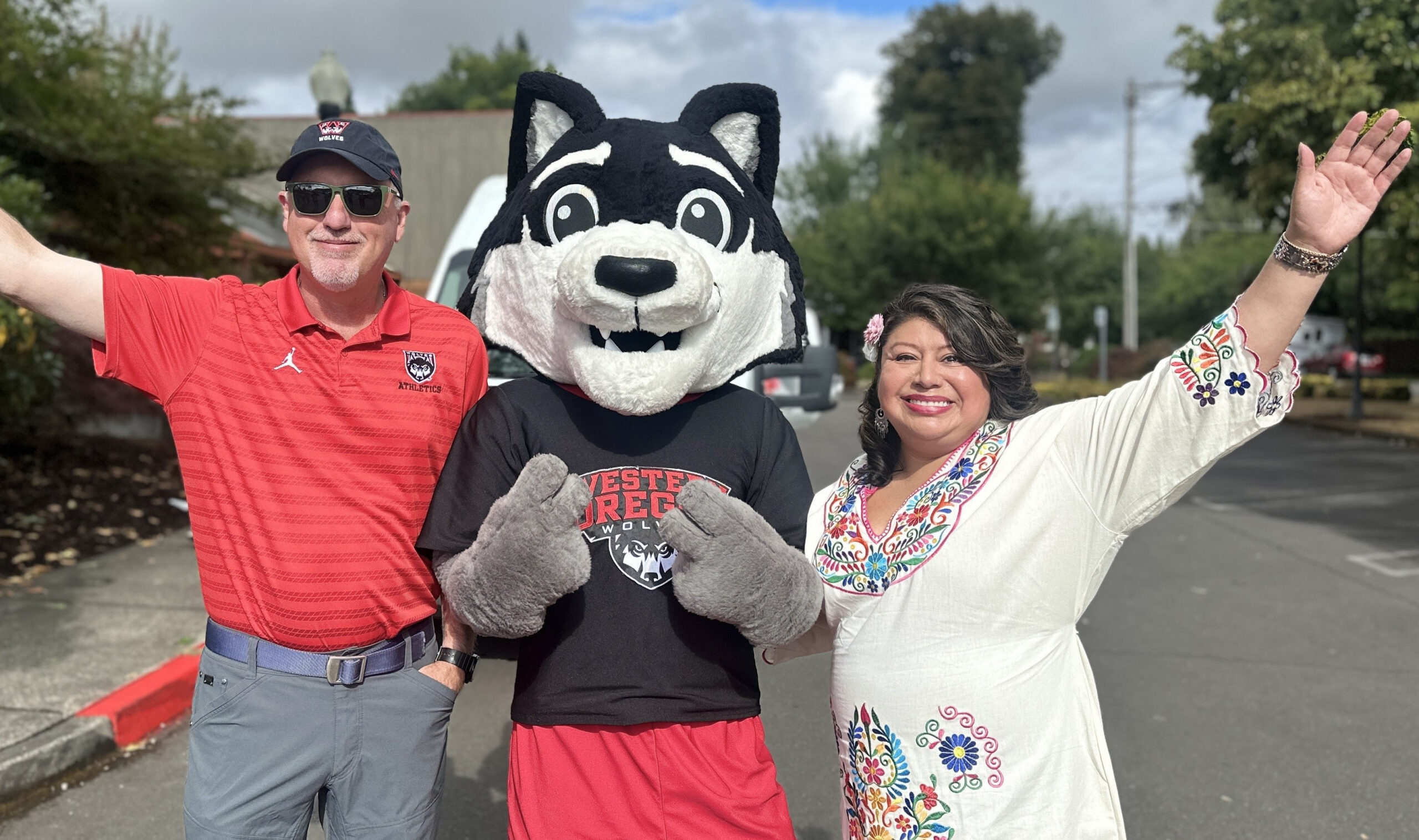 Two people standing next to a wolf mascot