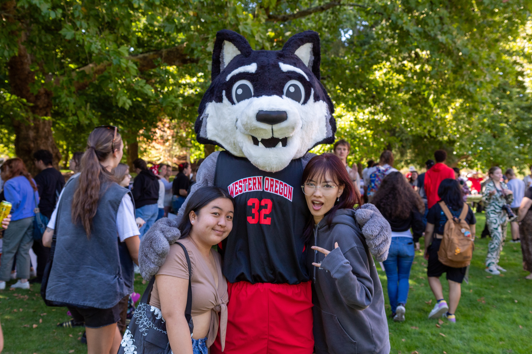 Two students hug and pose with WOU mascot, Wolfie.